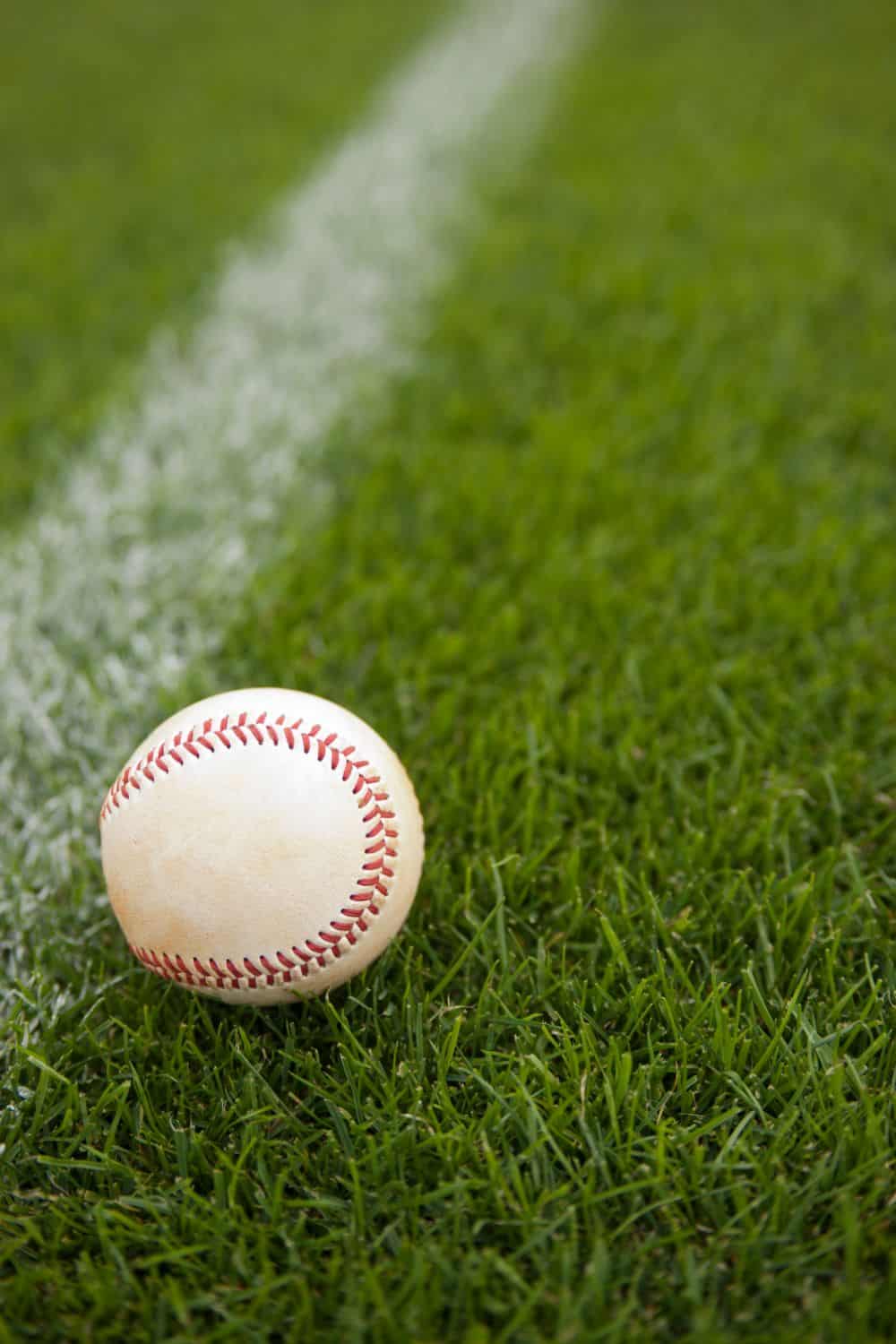 A baseball rests on lush green grass near a white foul line, evoking a scene from a baseball field perfectly maintained by Avondale Turf and Landscape.