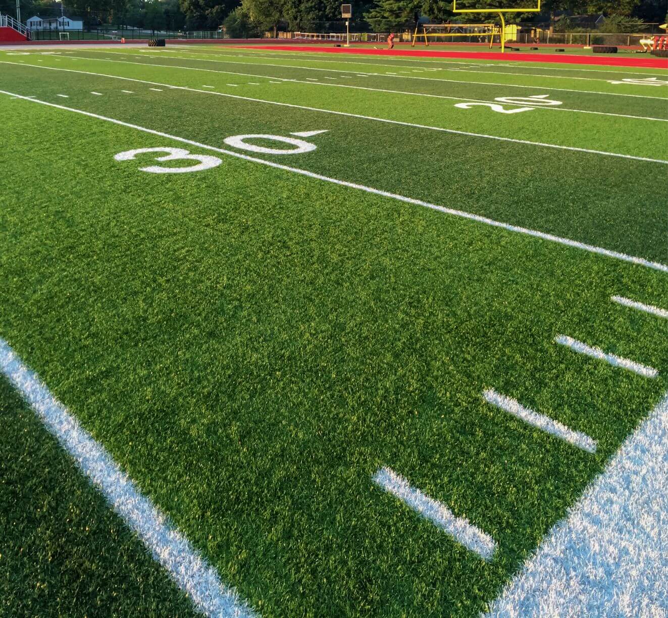A close-up view of the 30-yard line on a green football field, featuring Avondale Turf and Landscape’s expertly maintained grass, with white yard markings and a yellow goalpost visible in the distance under clear sunlight.