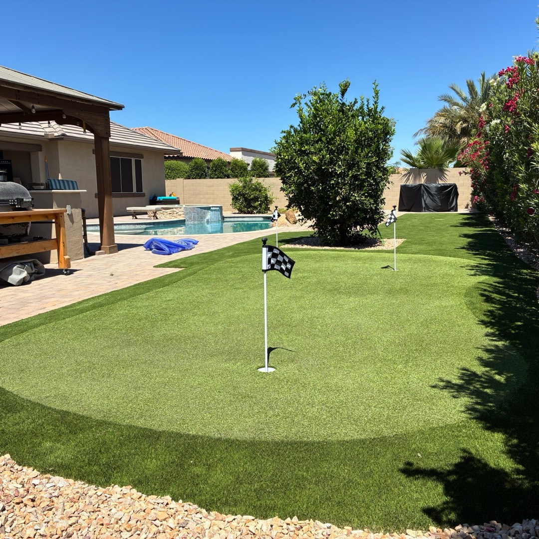 Backyard artificial turf putting green with two flags, curving around a pool and spa beside a paver patio and pergola